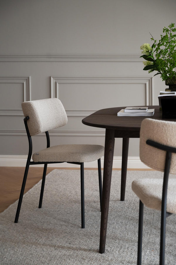 Beige stol med svarta ben vid mörkt matbord i modern matsal med ljusgrå vägg