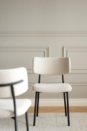 Cremevit stol med bouclétyg och svarta ben framför ljus väggpanel
