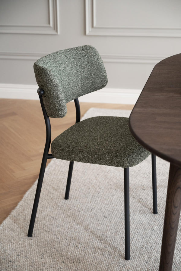 Grön stoppad stol med svarta metallben bredvid mörkt träbord på ljus matta