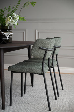 Gröna matstolar med armstöd och svarta ben vid matbord i modern skandinavisk stil