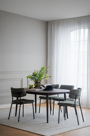 Matbord i mörkt trä med gröna stoppade stolar i ljust matrum med vita väggar och gardiner
