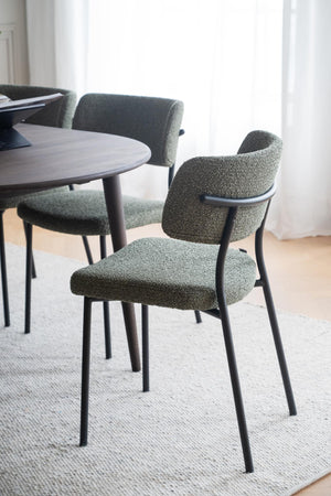 Gröna matstolar med bouclé-tyg och svarta metallben runt runt matbord i ljust rum