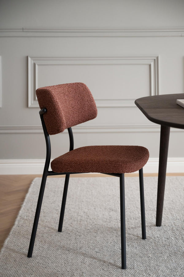 Brun stol med svarta metallben och bouclétyg bredvid mörkt träbord på ljus matta