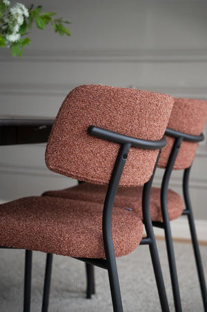 Stol med rödbrunt bouclé-tyg och svart metallram, närbild på ryggstöd och armstöd