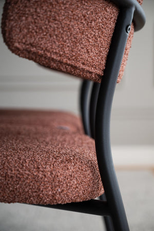 Stol med rosa bouclé-klädsel och svart metallram, närbild på sits och ryggstöd