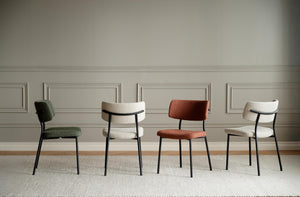 Fyra moderna matstolar med svarta metallben i grönt, beige, rostrött och vitt mot ljus vägg med pärlspont