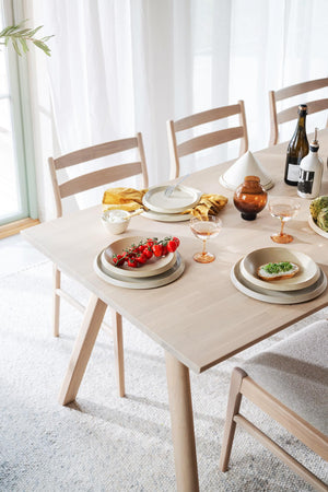 Ljust matbord i trä med stolar, dukad med tallrikar, glas och mat i skandinavisk stil