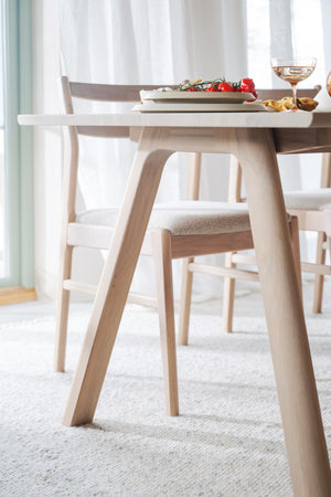 Ljust matbord i trä med skandinavisk design och matchande stolar, uppdukat med tallrikar och glas