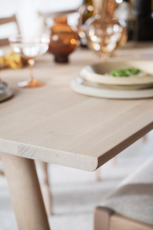 Ljust matbord i trä med dukade tallrikar, glas och dekoration i neutral färgpalett
