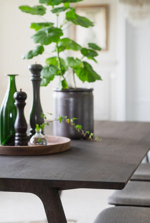 Mörkbrun trämatbord med rund bricka, grön glasflaska, svarta pepparkvarn och krukväxt i modern matsal