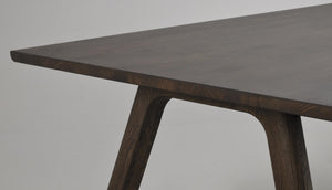 Närbild på mörkbrun träbordsskiva med snedställt ben i massivt trä med synlig åderstruktur