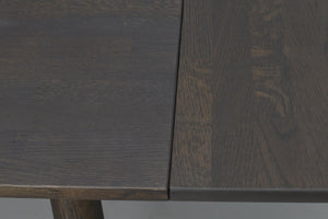 Närbild på mörkbrun träbordsskiva med utdragsfunktion som visar infälld skiva och naturlig trästruktur