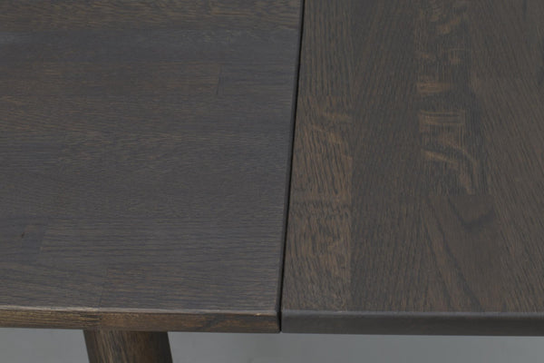 Närbild på mörkbrun träbordsskiva med utdragsfunktion som visar infälld skiva och naturlig trästruktur