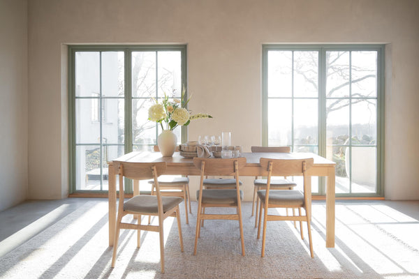 Matbord i ljust trä med stolar i skandinavisk stil, placerat i ljust matrum med stora fönster