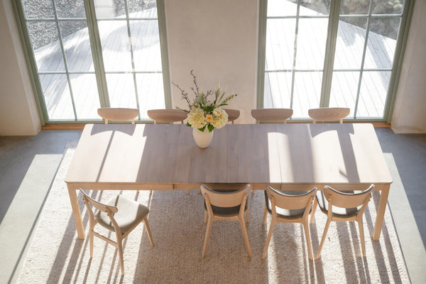 Matbord i ljust trä med matchande stolar i ljust matrum med stora fönster och vit matta