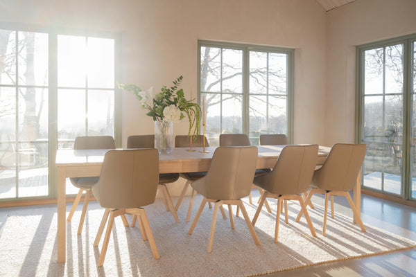 Matgrupp i ljust trä med åtta beige stolar i modern matsal med stora fönster och naturligt ljus