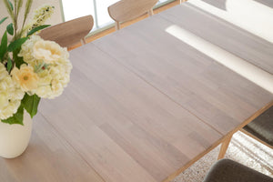 Ljust trägolv i modern matsal med bord, stolar och vita blommor i vas