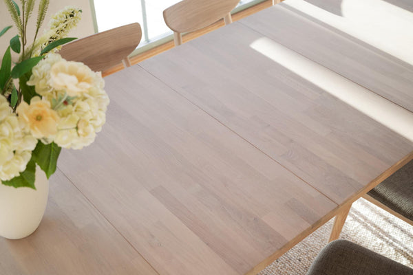 Ljust trägolv i modern matsal med bord, stolar och vita blommor i vas