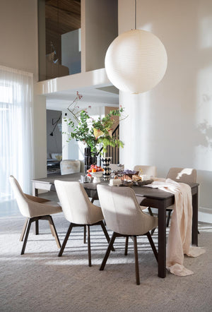 Modern matplats med rund vit taklampa, mörkt matbord, beige stolar och gröna växter som dekoration