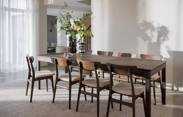 Matbord i mörkt trä med åtta stolar i vardagsrum med vita gardiner och växtdekoration