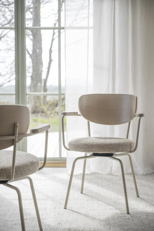 Moderna stolar med trärygg och textilklädsel vid fönster i ljust rum med vita gardiner