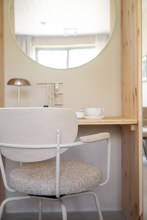Minimalistisk arbetsplats med ljust trä skrivbord, modern stol med beige sits och rund spegel på väggen