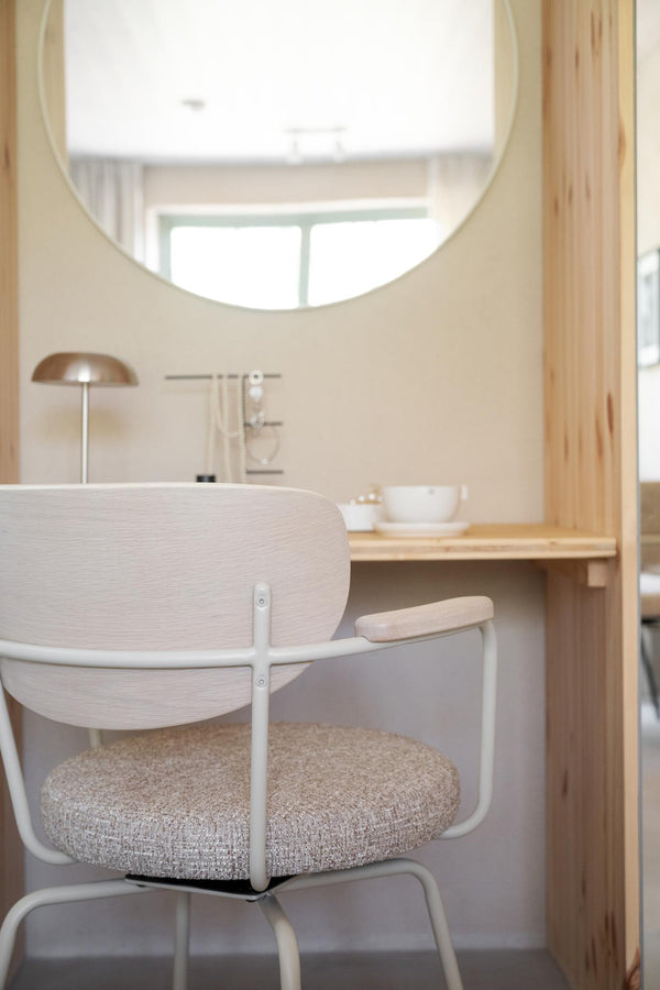 Minimalistisk arbetsplats med ljust trä skrivbord, modern stol med beige sits och rund spegel på väggen