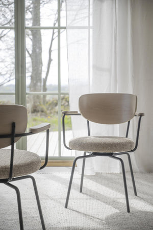 Moderna matstolar med armstöd, ljust träryggstöd och grå klädsel på metalben vid fönster