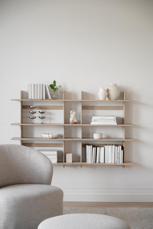 Väggmonterad bokhylla i ljust trä med böcker och dekorativa föremål i minimalistisk stil