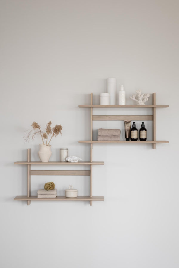 Träväggställ i ljust trä med badrumsartiklar, handdukar och dekorativa detaljer mot ljus vägg