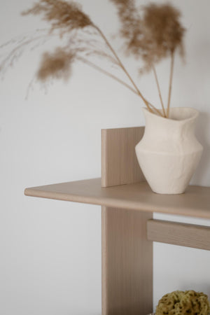 Ljust träbord med vit keramisk vas och torkade gräs i minimalistisk skandinavisk inredningsstil