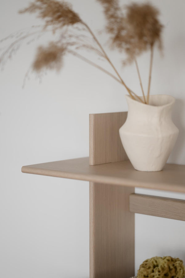 Ljust träbord med vit keramisk vas och torkade gräs i minimalistisk skandinavisk inredningsstil