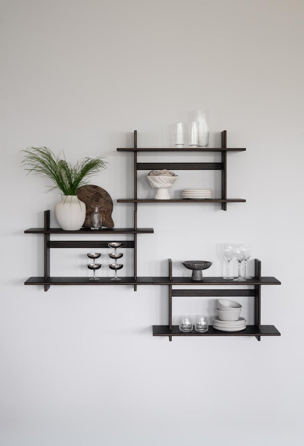 Moderna vägghyllor i mörkt trä med asymmetrisk design, dekorerade med vaser, glas och keramik mot ljus vägg