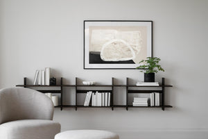 Svart väggmonterad hylla med böcker och dekoration under abstrakt tavla i minimalistisk vardagsrumsinredning