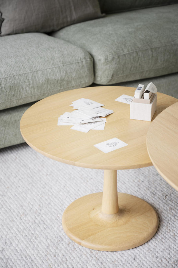 Runt soffbord i ljust trä med vita visitkort och pennor framför grå soffa