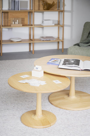 Satsbord i ljust trä med runda skivor och pedestal, stylat med böcker och dekoration i skandinavisk inredning