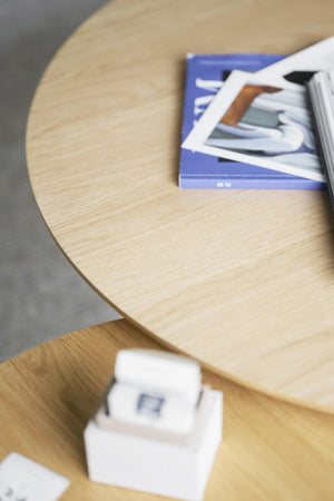 Runt soffbord i ljust trä med blå bok och vita dekorationer på hylla