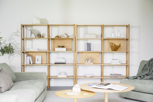 Ljus bokhylla i trä med böcker och dekorationer, flankerad av gröna soffor i minimalistiskt vardagsrum