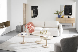 Modernt vardagsrum med vit soffa, runda soffbord i trä och minimalistisk inredning i ljusa toner