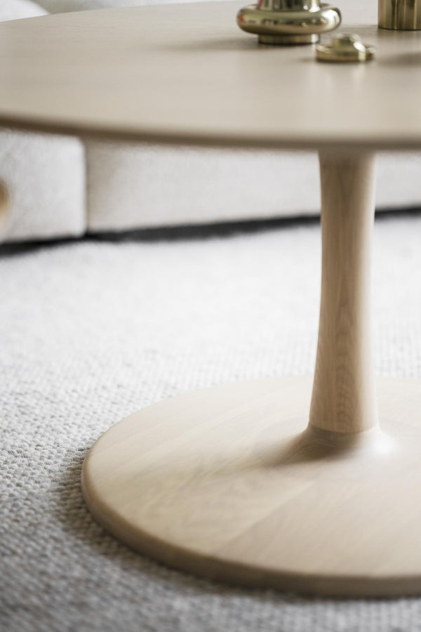 Soffbord med rund beige bordsskiva och smal konisk fot på ljus matta i modern skandinavisk stil