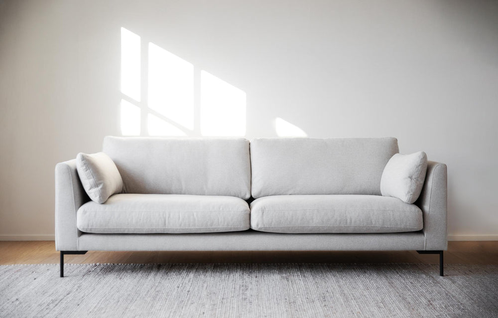 Beige tvåsits soffa med svarta metallben och cylindriska armstöd mot vit bakgrund