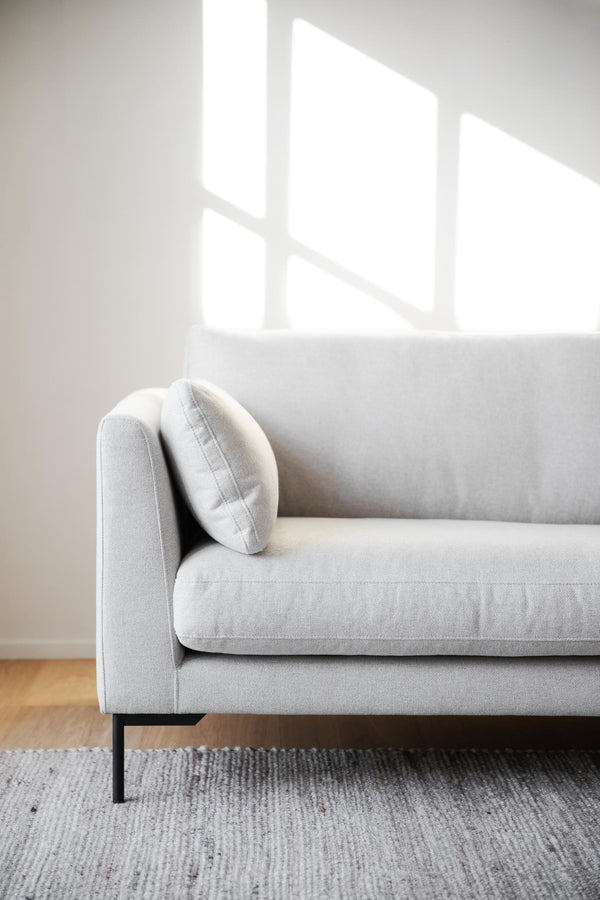 Ljusgrå soffa med kudde i minimalistiskt vardagsrum med trätrall och matta