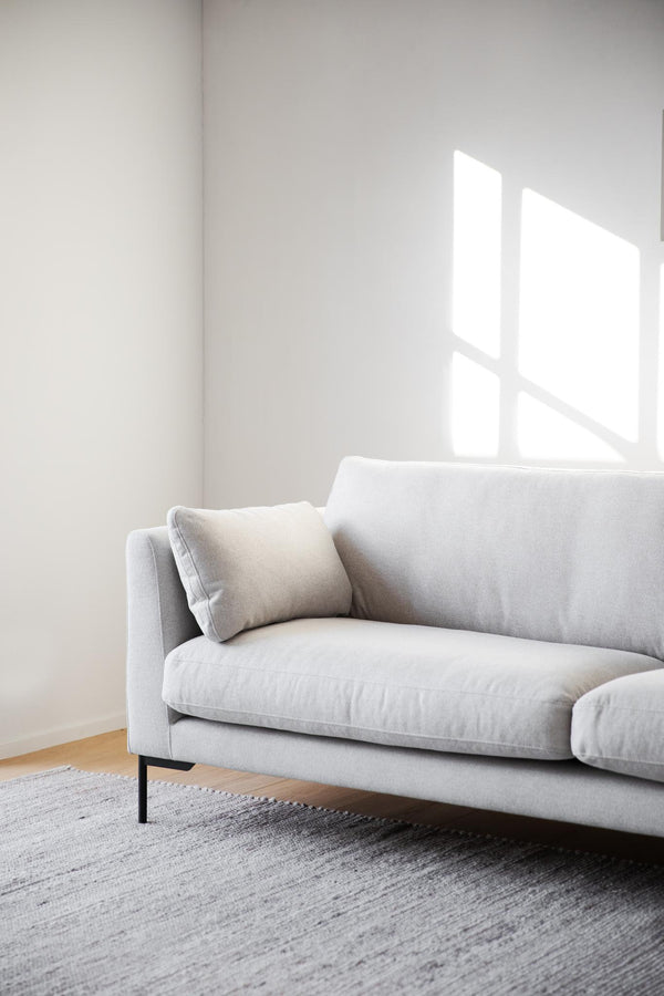 Ljusgrå soffa med dyna på strutmönstrad matta i minimalistiskt vardagsrum med vita väggar