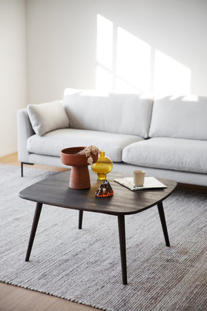 Modernt vardagsrum med grå soffa, mörkt soffbord med terrakottaskål och gul vas på ljus matta
