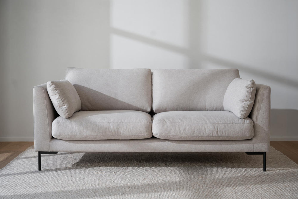 Beige tvåsitssoffa med svarta metallben och två cylindriska kuddar, modern design