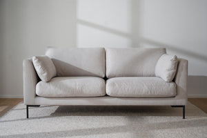 Ljusgrå tvåsitssoffa med svarta metallben och två kuddar på ljus matta i minimalistiskt rum