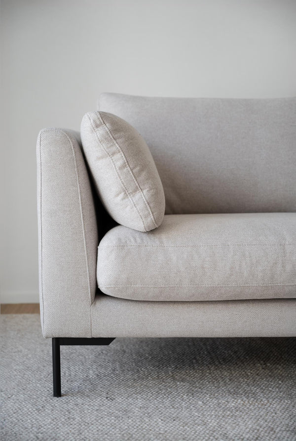 Beige soffa med loose fit-klädsel och svarta metallben på grå matta mot ljus vägg