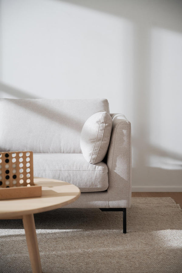 Beige linnefåtölj med rundad armstöd bredvid ljust träbord i minimalistisk vardagsrumsinredning