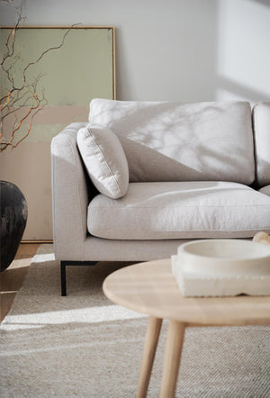 Ljusgrå tygsoffa med kuddar och svarta metallben i modernt vardagsrum med neutala toner