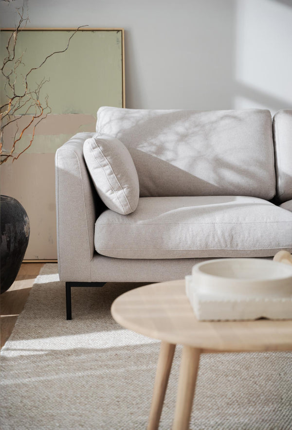 Ljusgrå tygsoffa med kuddar och svarta metallben i modernt vardagsrum med neutala toner